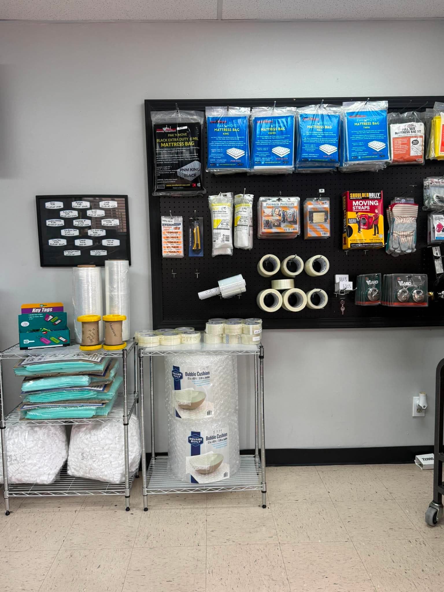 Moving supplies including mattress bags, bubble wrap, and tape displayed on a pegboard and shelves.