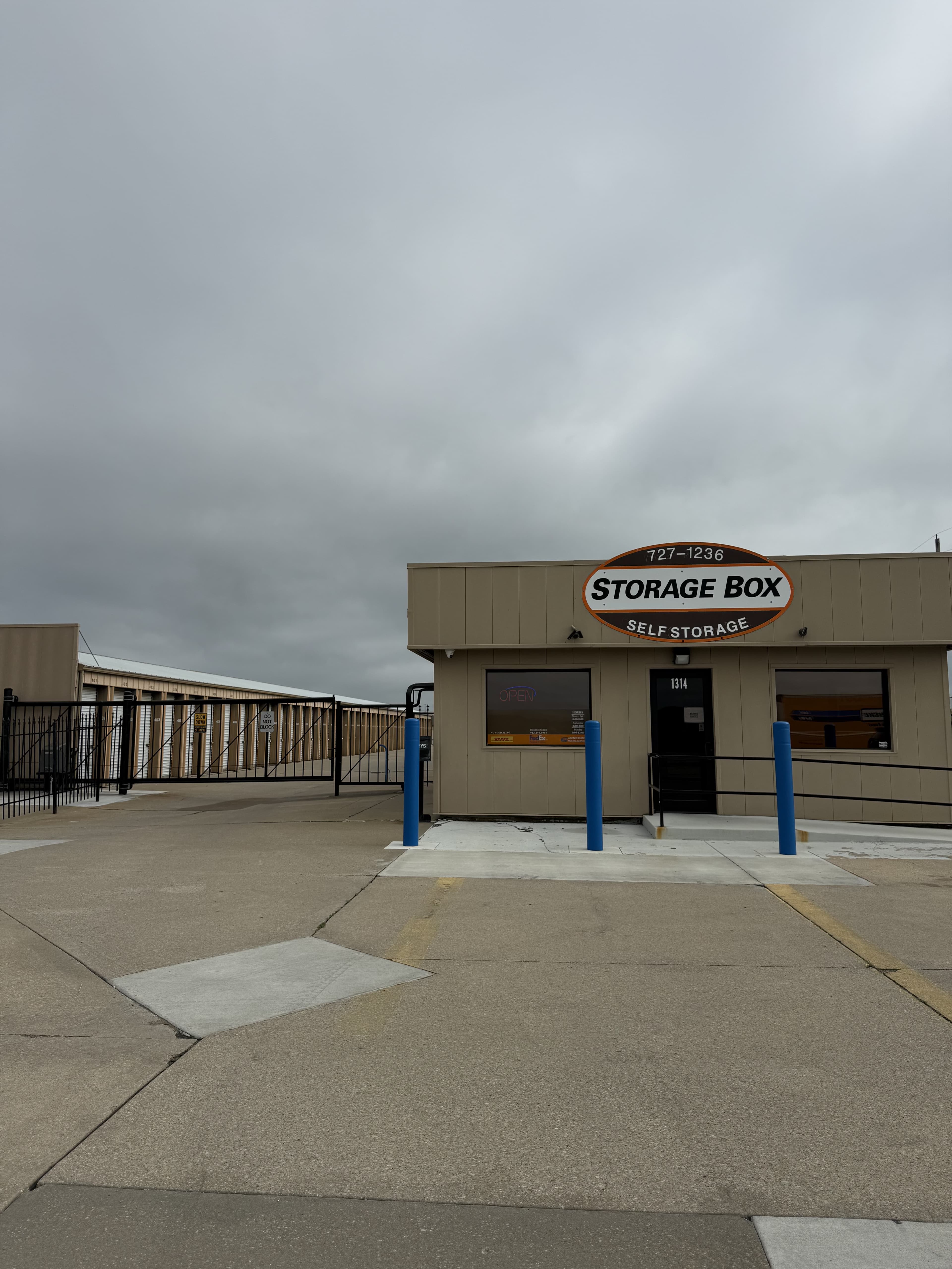 Tan Storage Box office building with gated storage units under a grey, overcast sky.